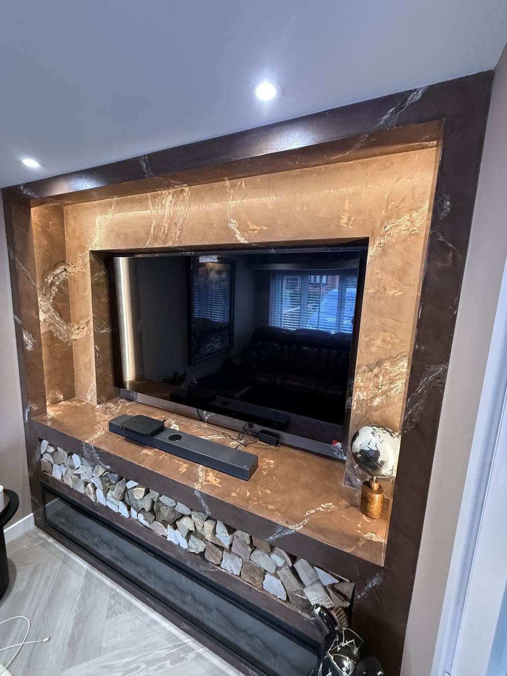 Copper marble-effect media wall with LED-lit recess and log store